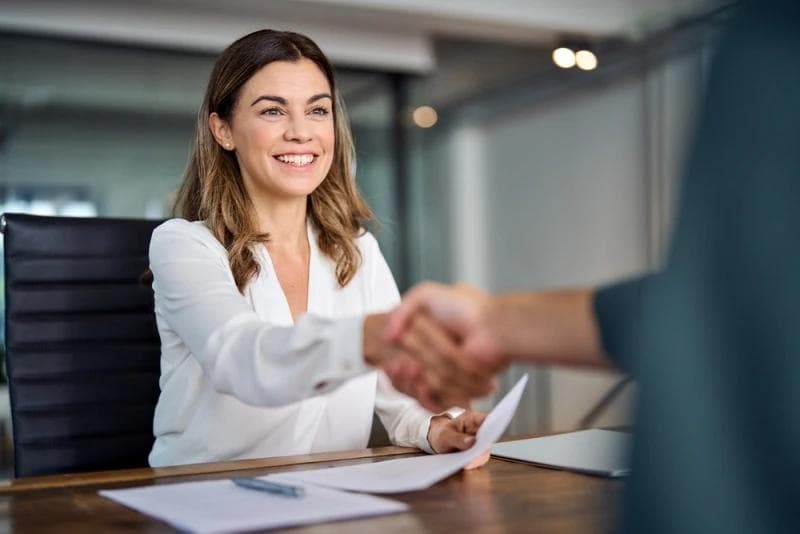 Woman smiling and shaking hands with executive after signing pre-settlement funding documents