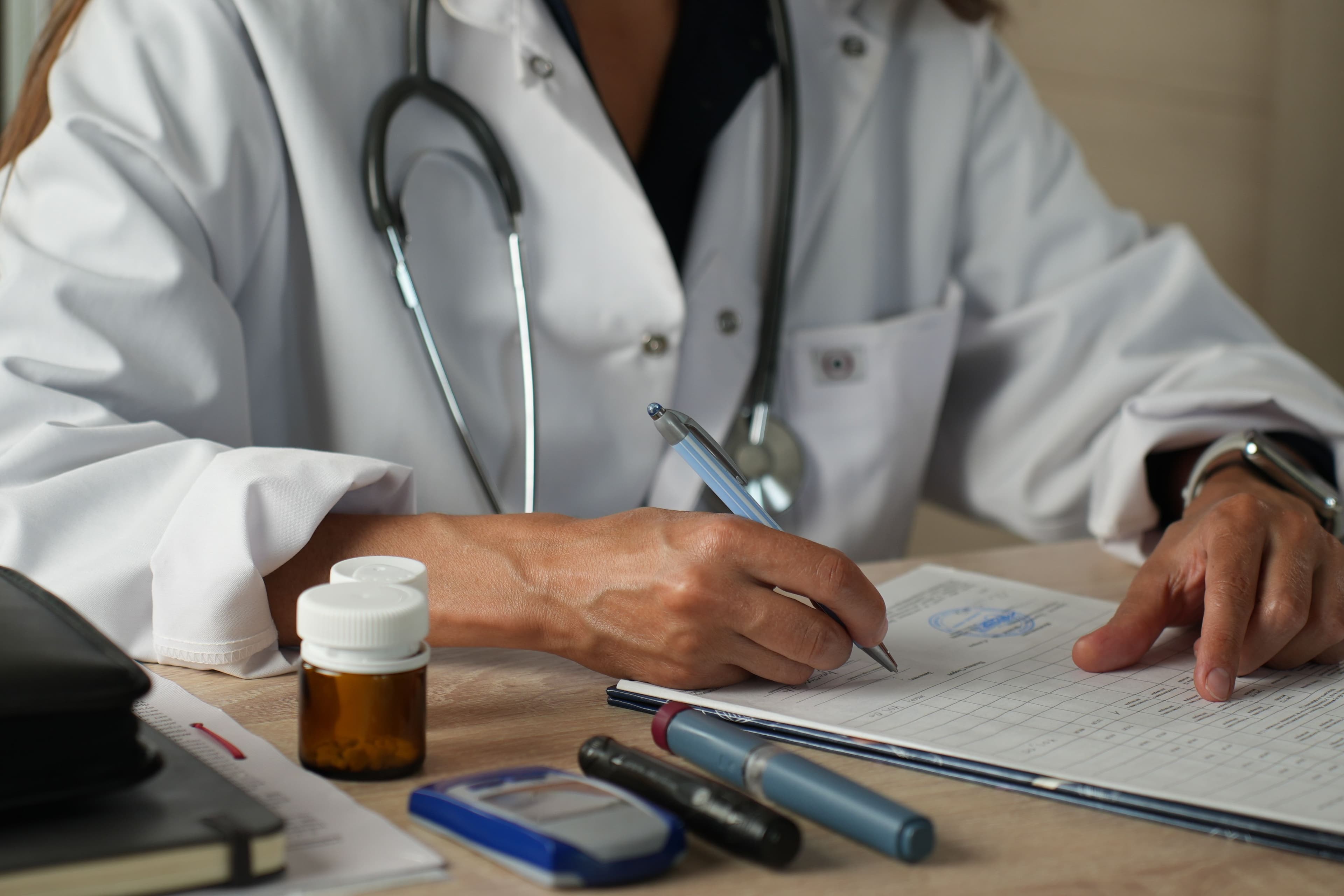 Close-up of a doctor writing medical documentation at a desk with papers and prescription medication.