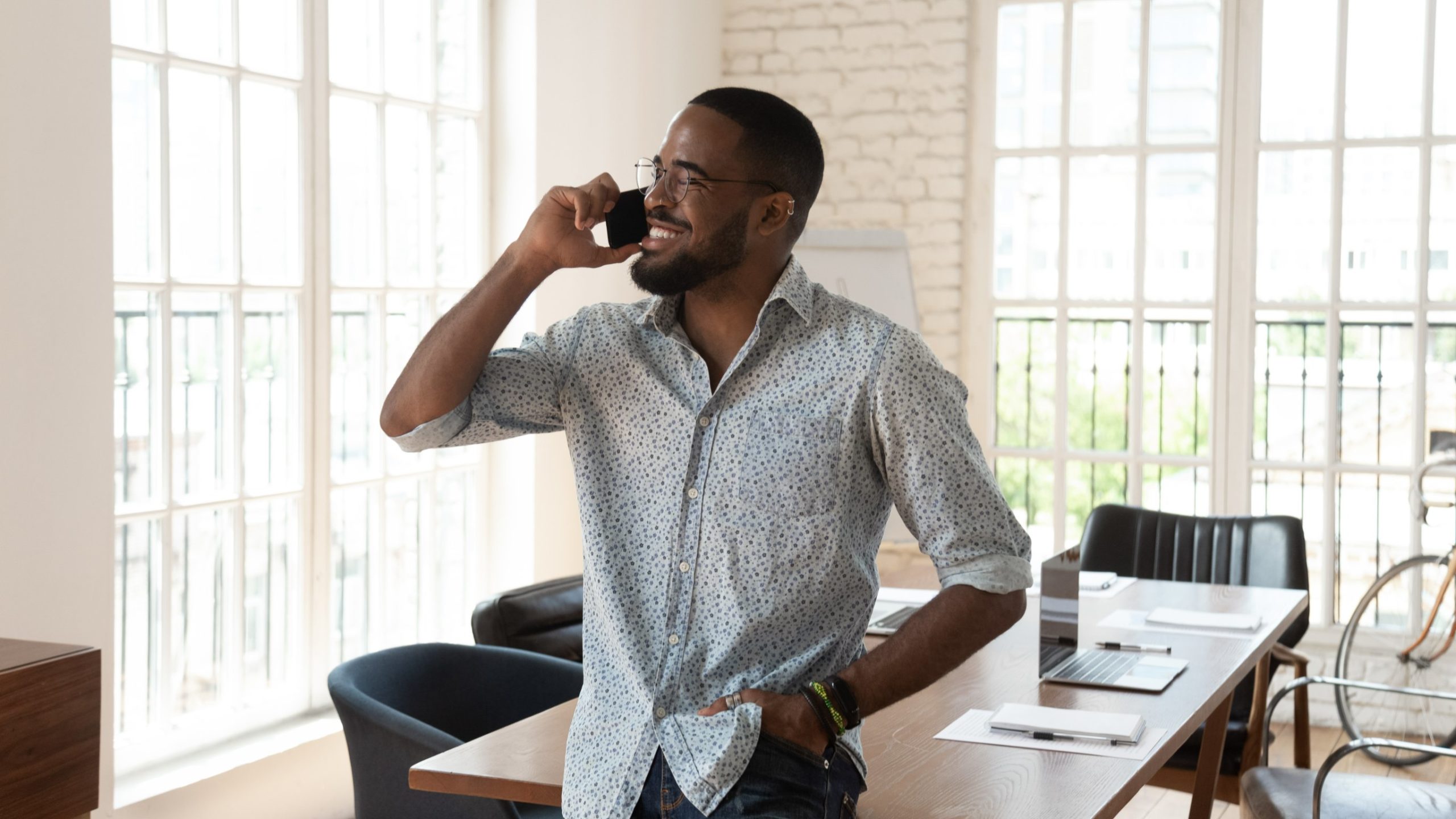 A man casually leaning on a desk talking on the phone. He is smiling. He is happy and satisfied with his experience with Rockpoint Legal Funding.
