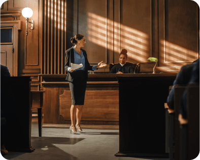 Case Cost Funding. A female attorney stands in a courtroom, before a judge. She appears to be addressing a person outside of the frame, who may be a witness. Rockpoint Legal offers pre-settlement case cost funding.