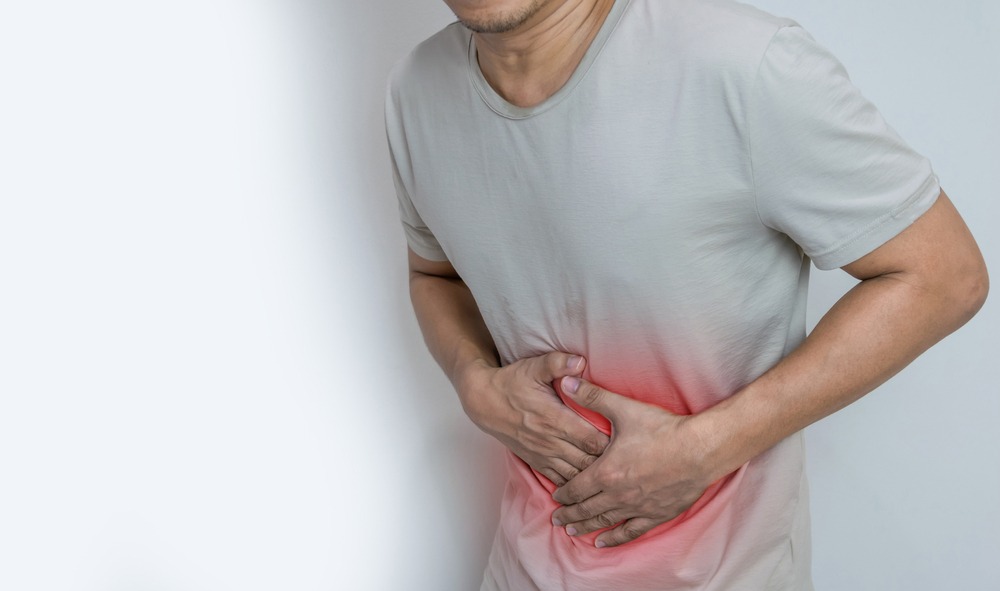 An image of a man against a white background, visible from the hips to the chin. He is holding his abdomen with both hands and slightly bent over. The area under his hands is artificially enhanced to show a red glow where the man's hands are meeting his belly to indicate pain.