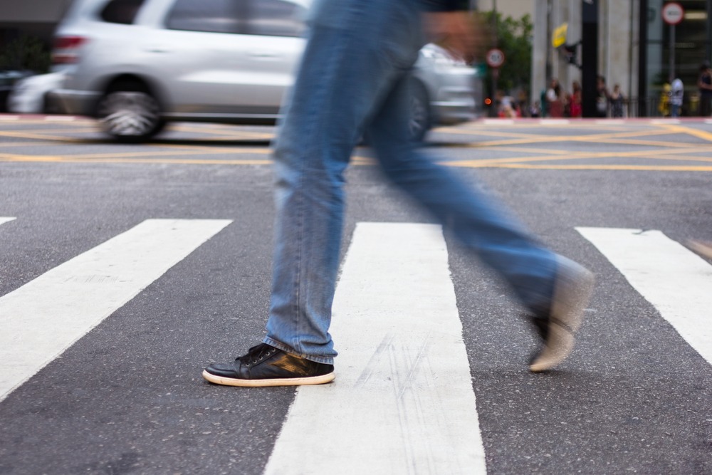 An image of a man, viewed from the waist down, crossing the street in the crosswalk. Rockpoint Legal Funding provides cash for plaintiffs injured by commercial vehicles.